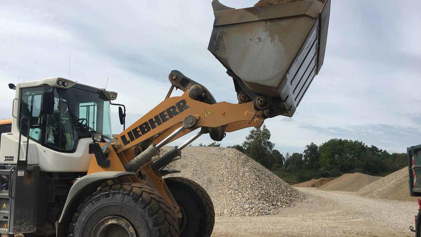 En stor gravemaskine fra Liebherr løfter en skovl med grus på en byggeplads.