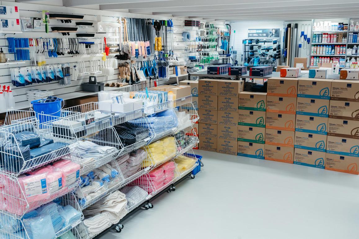 Butik med rengøringsartikler og opbevaringskasser, organiseret på hylder og i kasser i et lyst rum.