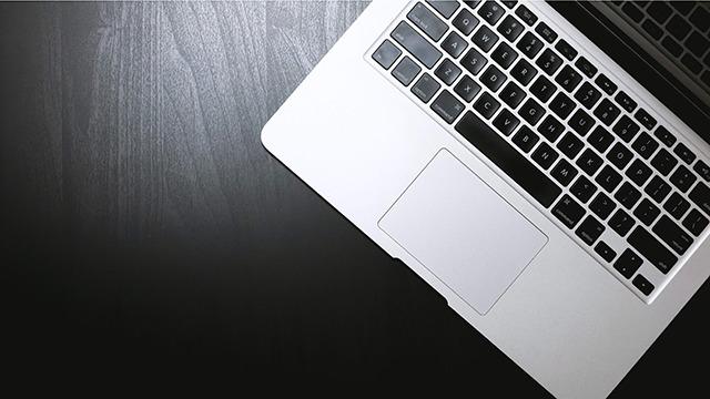 En bærbar computer med sort tastatur og touchpad på et mørkt træbord.