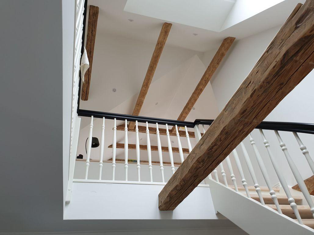 Indvendig trappe med synlige træbjælker og hvidt gelænder i moderne husdesign.