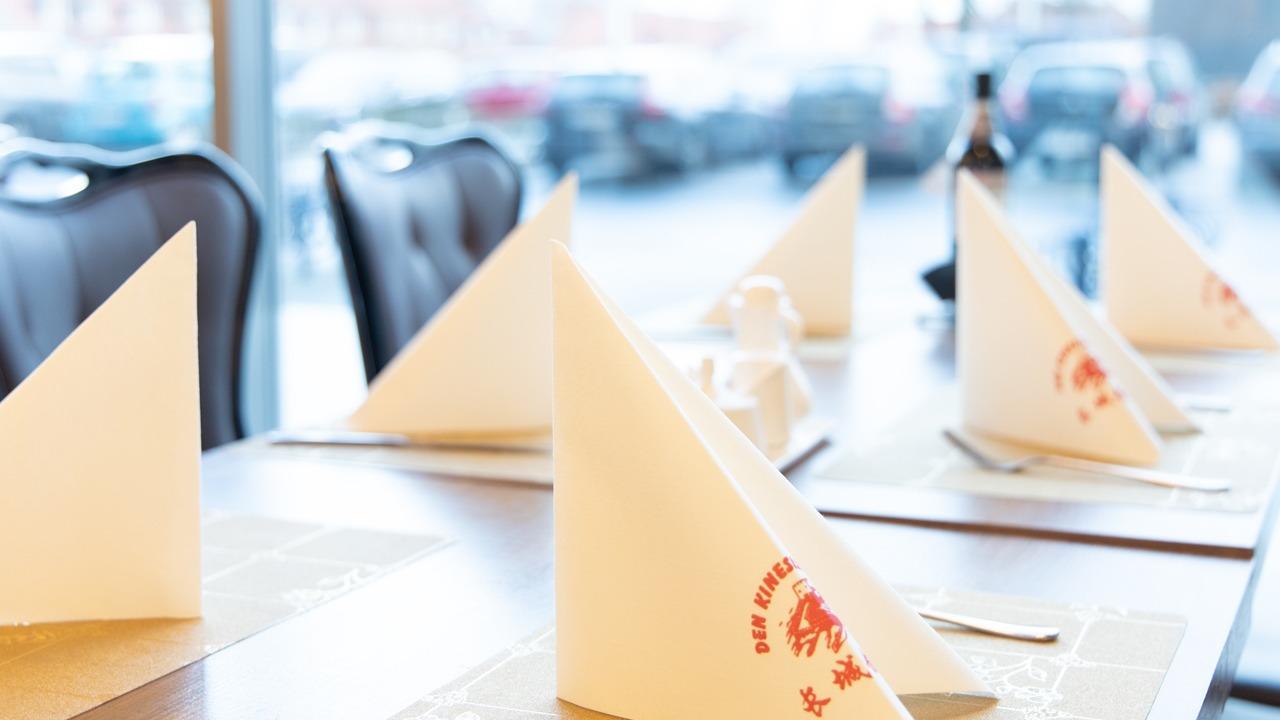 Borddækning med hvide servietter i spidse former og menukort på et restaurantbord.