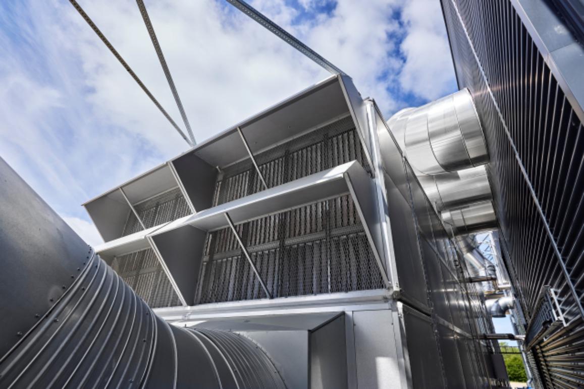 Billede af en stor ventilationsenhed med metalgitter og rør, der strækker sig mod en blå himmel.