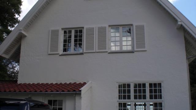 Hvidt hus med røde tagsten og vinduer med skodder, beliggende i et roligt område.