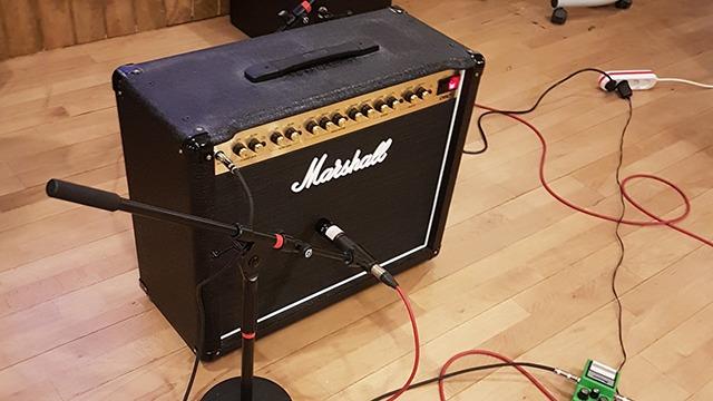 En Marshall guitarforstærker med mikrofon og effektpedal i et musikstudie med trægulv.