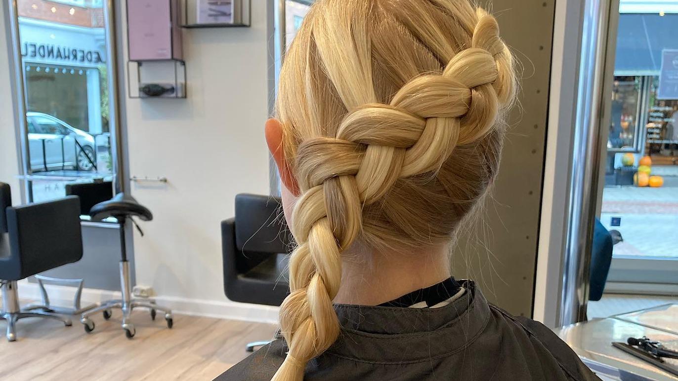 En pige med en flot fletning i lyst hår, der sidder i en frisørsalon.