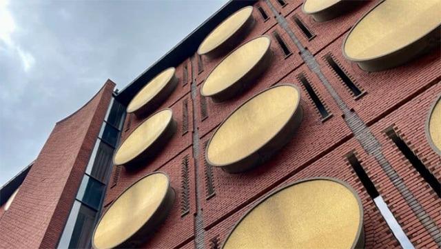 Facaden af en bygning med store, runde, gyldne elementer og mursten i rød farve under en grå himmel.