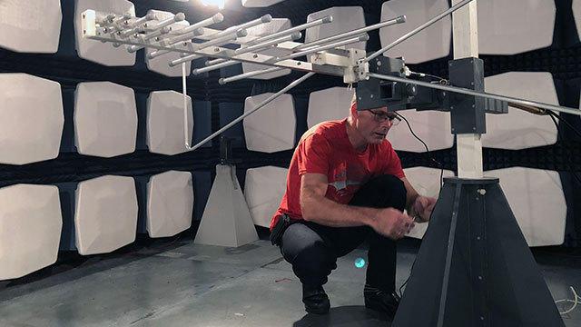 En mand i rød t-shirt justerer en antenne i et akustisk testmiljø med lydabsorberende paneler.