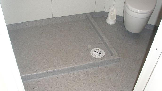 Badeværelse med grå fliser, toilet og bruseområde med afløb i gulvet.