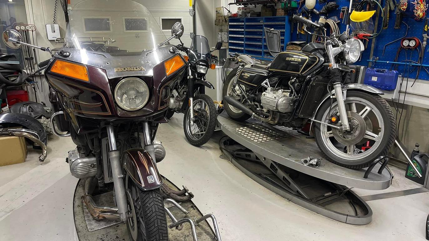 To motorcykler i et værksted, en mørkebrun touringmotorcykel og en sølvfarvet klassisk motorcykel.