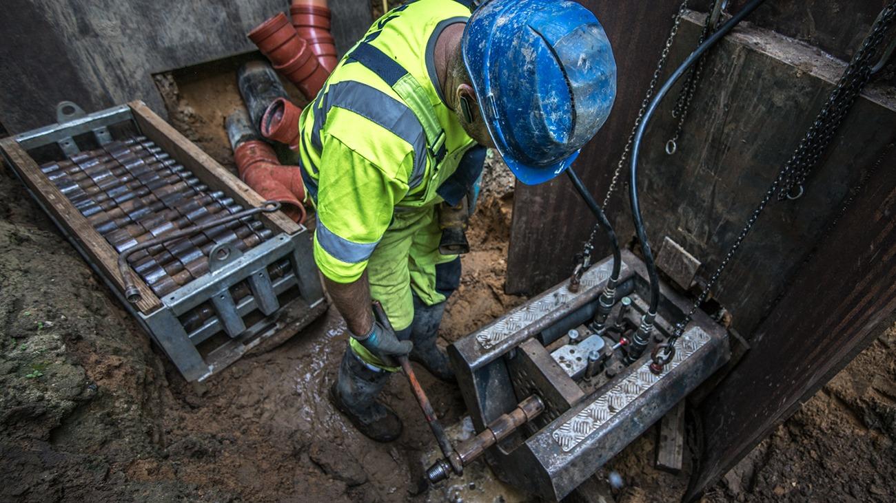 En arbejder i sikkerhedstøj og hjelm, der bruger en hammer til at arbejde på en byggeplads.