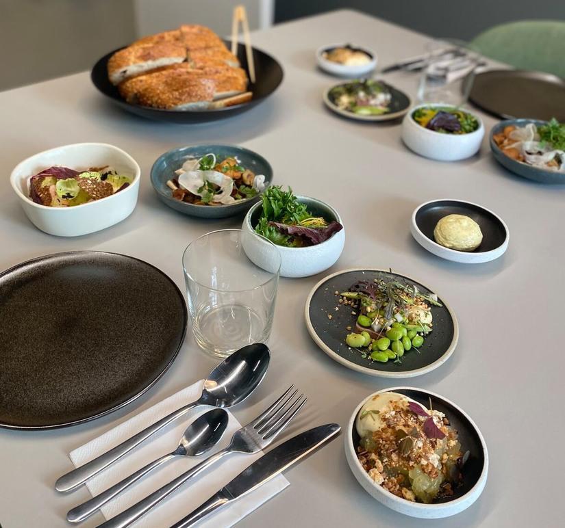 Et bord dækket med forskellige retter, herunder salater, fisk og brød, samt bestik og glas.