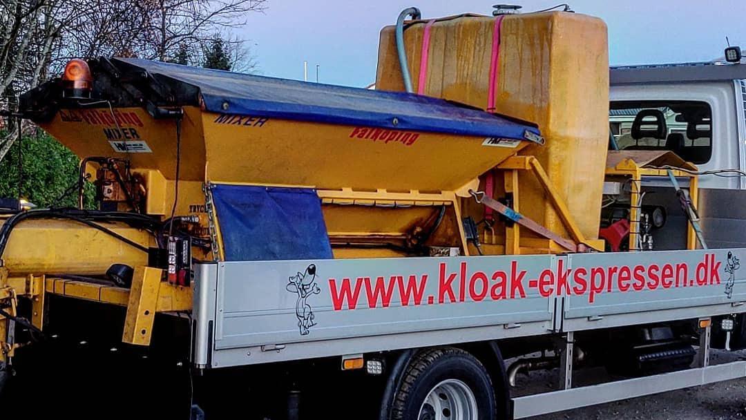 Gul kloakspilser med stor tank og hjemmeside på siden af en lastbil.