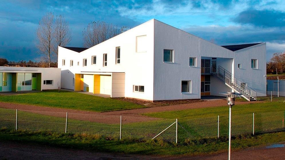 Moderne hvid bygning med store vinduer og en græsplæne foran, omgivet af et hegn.