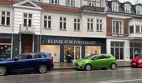 Klinik for fodterapi facade med biler parkeret på gaden i regnvejr.