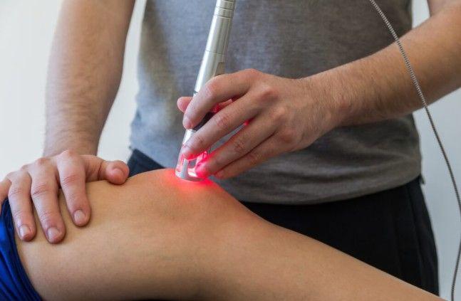 En terapeut bruger en laserbehandling på en patients knæ for at lindre smerte og fremme heling.