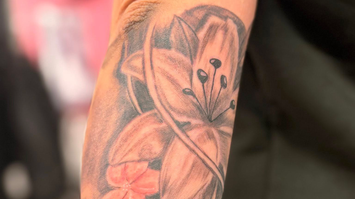 En detaljeret tatovering af en blomst på en arm, med nuancer af sort og grå.