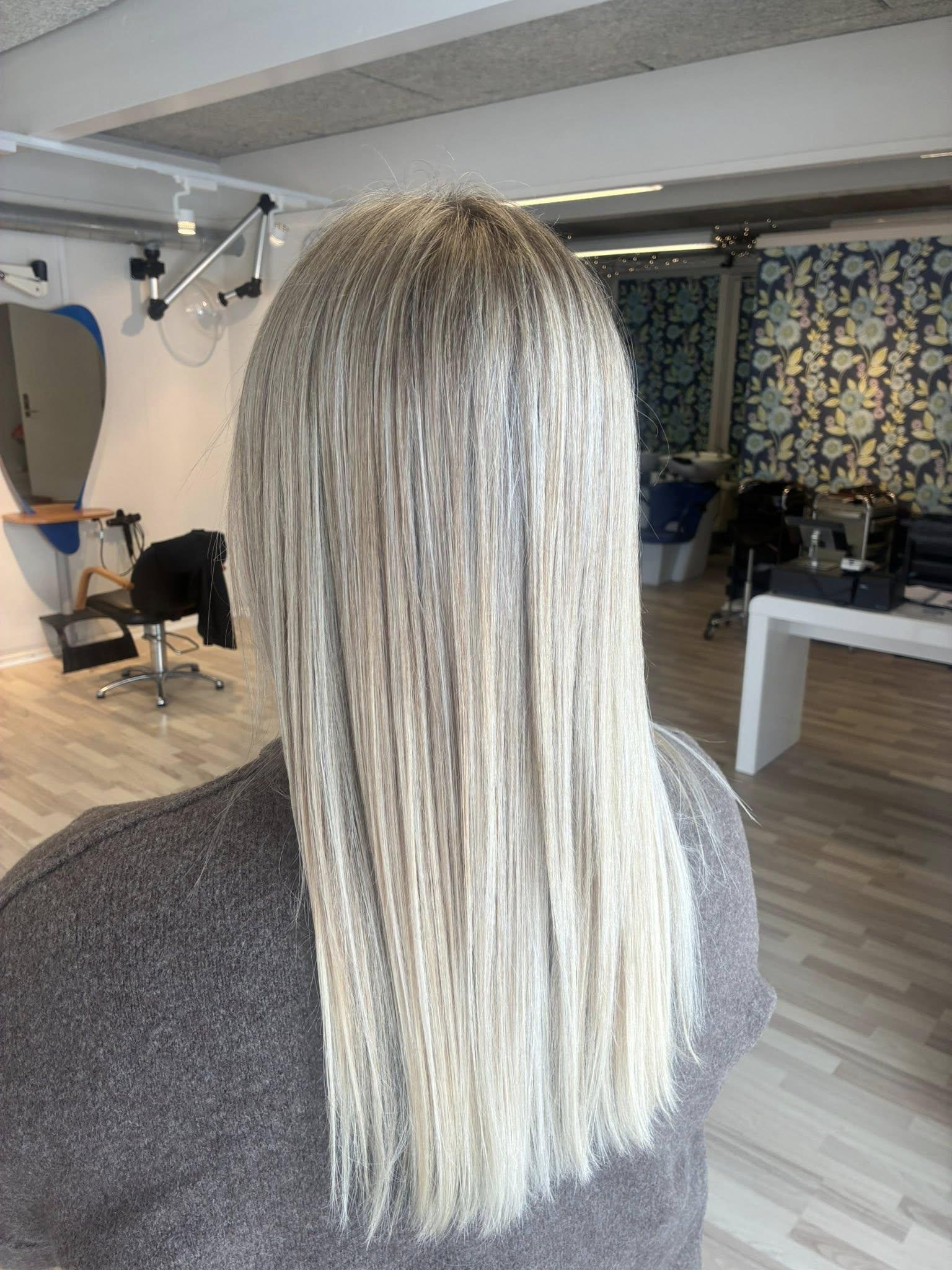 Langt, glat, lyst hår set bagfra i en frisørsalon med moderne indretning.