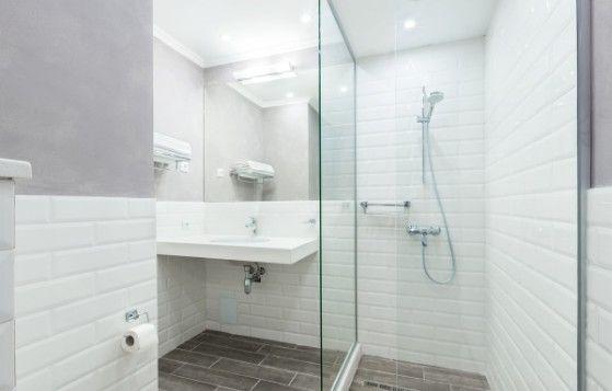 Moderne badeværelse med glasbruser, hvid flisevæg og minimalistisk indretning.