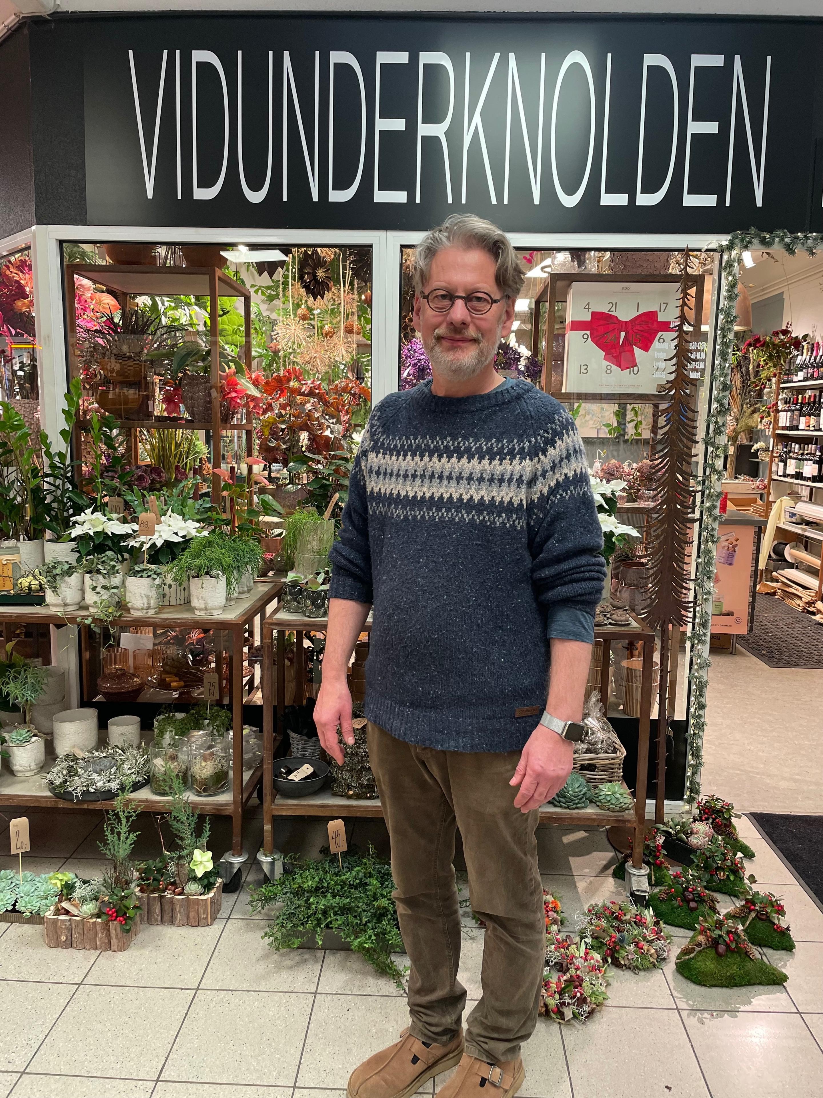 Mand står foran en blomsterbutik med navnet "Vidunderknolden" og omringet af planter og blomster.