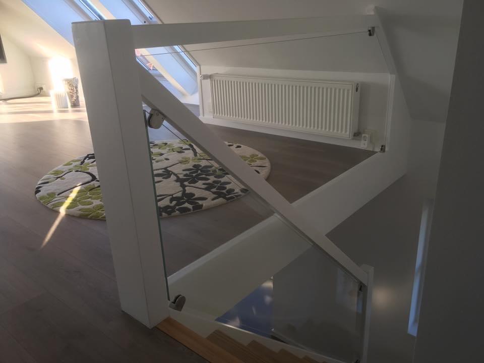 Moderne trappe med glasgelænder og radiator i en lys stue med et farverigt tæppe.