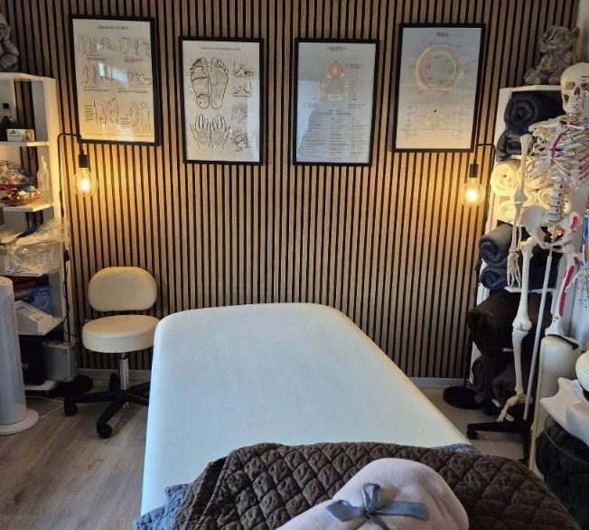 Behandlingsrum med en massagebriks, væg med kunstværker og en anatomisk model af et skelet.