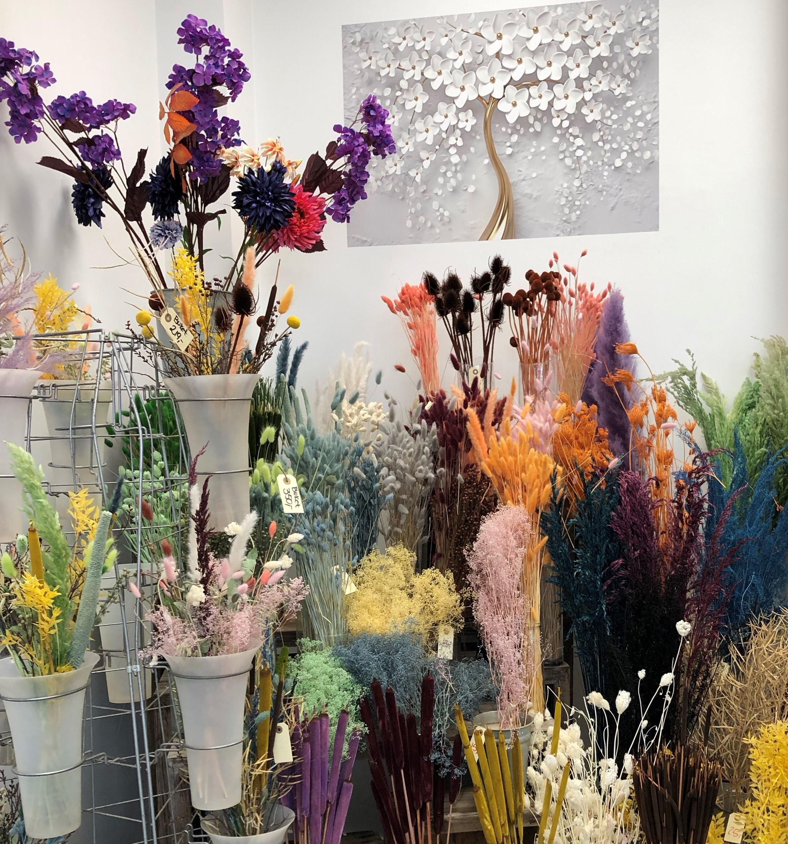 En farverig blomsterbutik med forskellige tørrede blomster i vaser og en kunstnerisk vægdekoration.