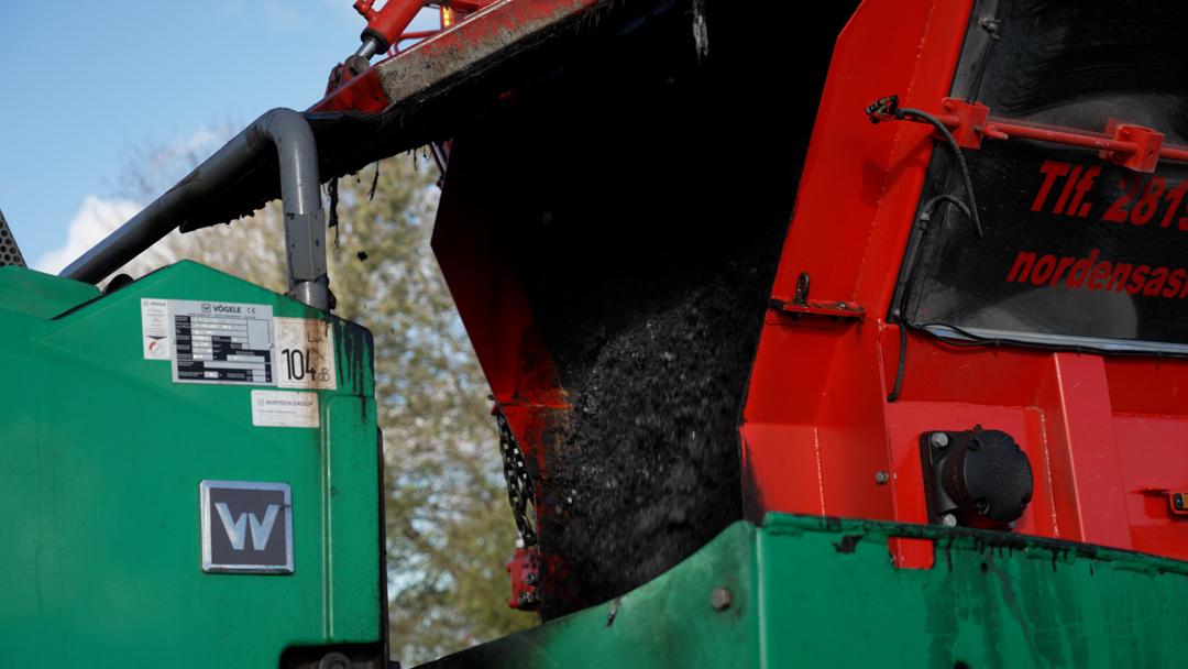 Affaldscontainer, der tømmer indholdet i en stor grøn skraldebil med rød bagklap.