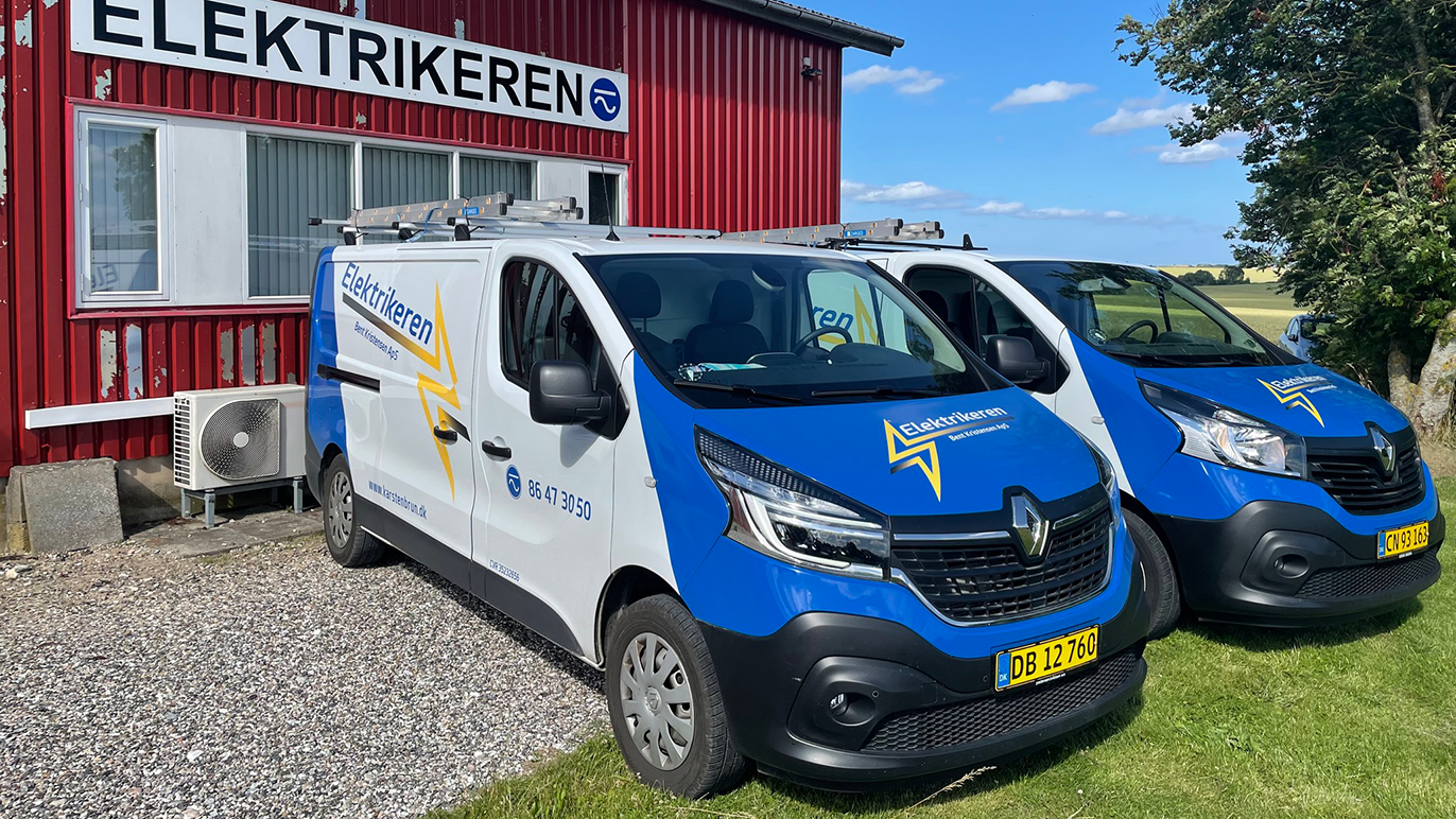 To biler med virksomhedens logo parkeret foran en rød bygning med skiltet "Elektrikeren".