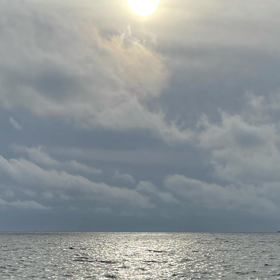 Solskin over havet med mørke skyer i baggrunden, der reflekterer lys på vandets overflade.