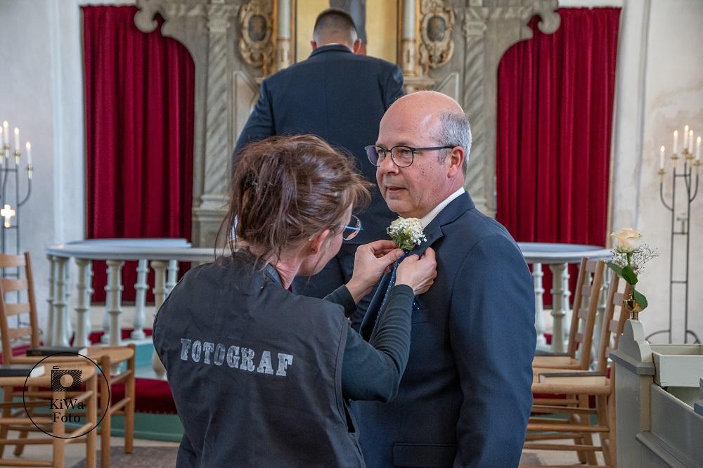 En fotograf sætter en blomst på en mand i jakkesæt i en kirke med røde gardiner.