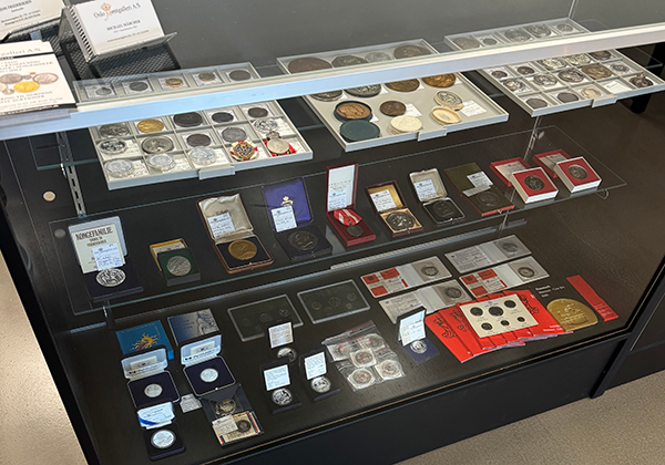 Vitrineskab med samling af mønter og medaljer, herunder forskellige numismatiske genstande og prisskilt.
