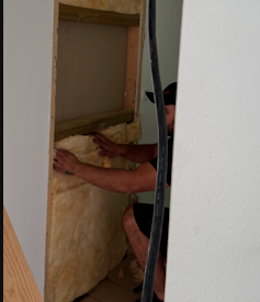 En håndværker installerer isolering i en væg i et rum.