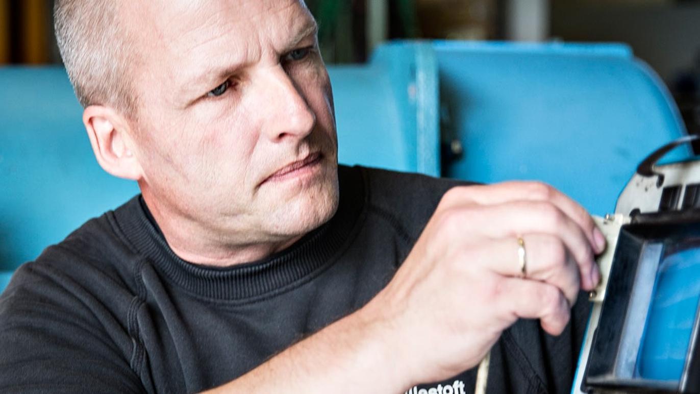 En mand arbejder koncentreret med en elektrisk enhed i et værksted.