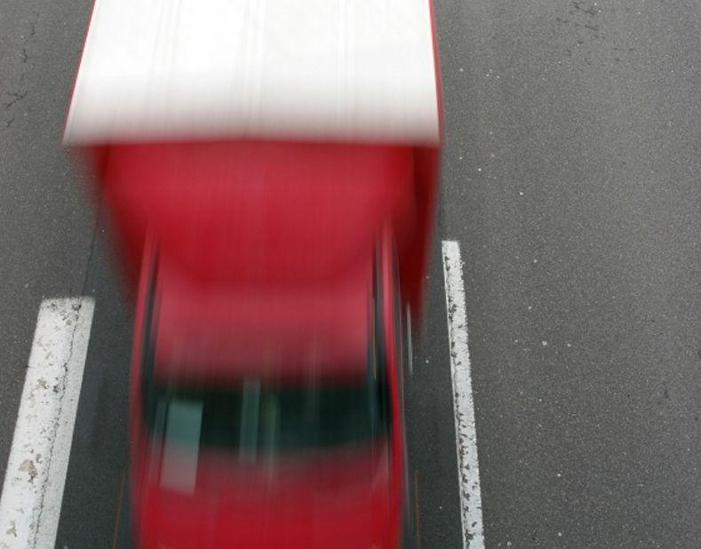 Rød lastbil, der kører hurtigt på en grå vej med hvide striber.