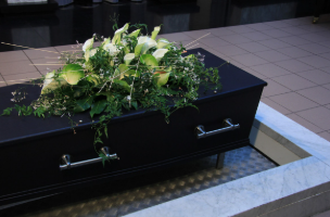 En sort kiste med blomsterarrangement og grønne planter på toppen, placeret i et rum med marmor- og flisegulv.