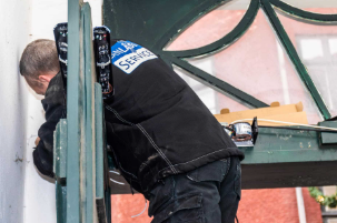 En tekniker arbejder på en bygning, mens han står på en stige med værktøj og øl i ryggen.