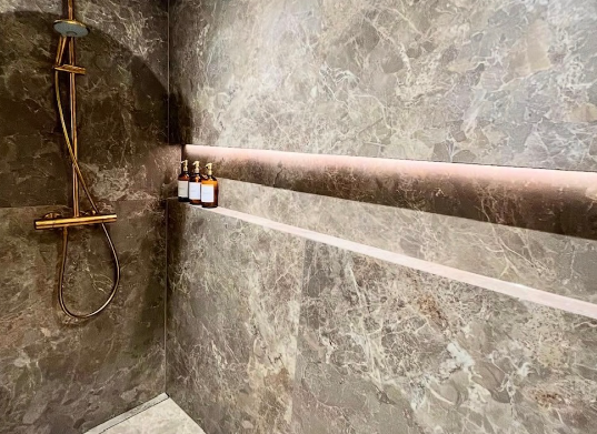 Moderne brusekabine med marmorvægge og tre flasker på en hylde i bronze.