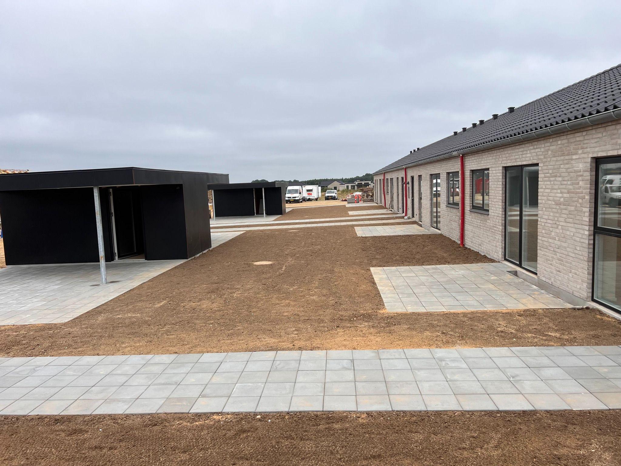 Nybygget boligområde med grusbelægning og moderne bygninger under en grå himmel.