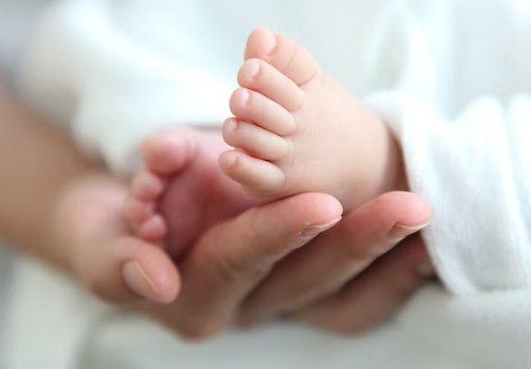 En hånd holder en lille babys fod med bløde tæer, omgivet af en hvid klud.