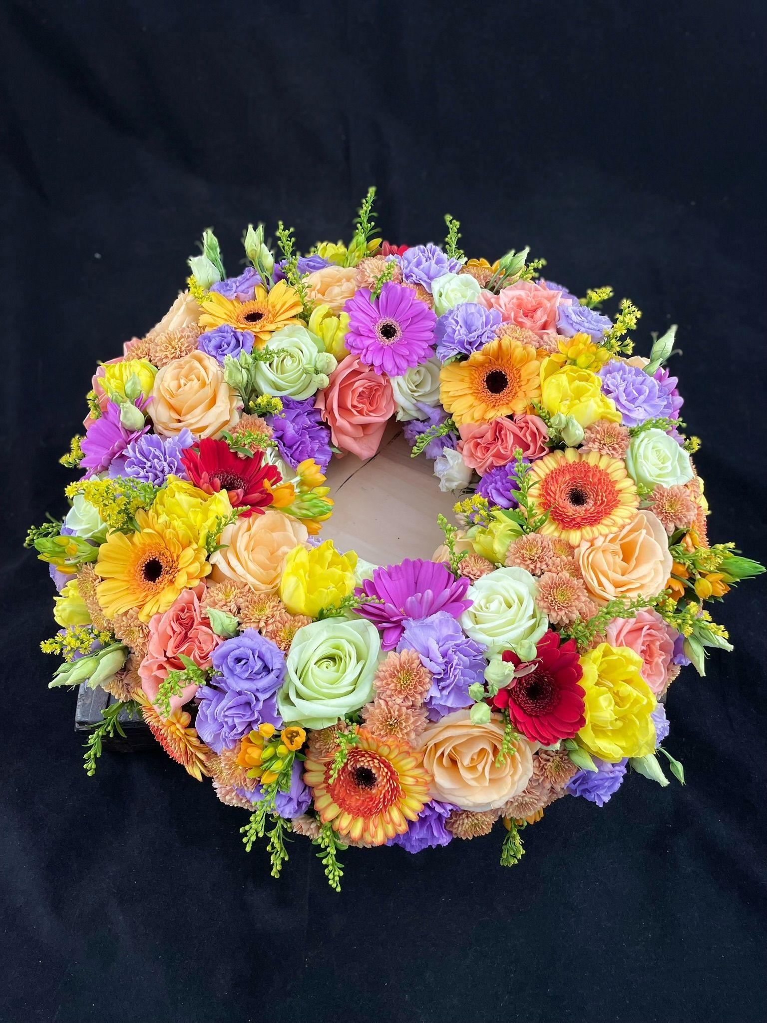En farverig blomsterkrans med roser, gerberaer og liljer på en sort baggrund.