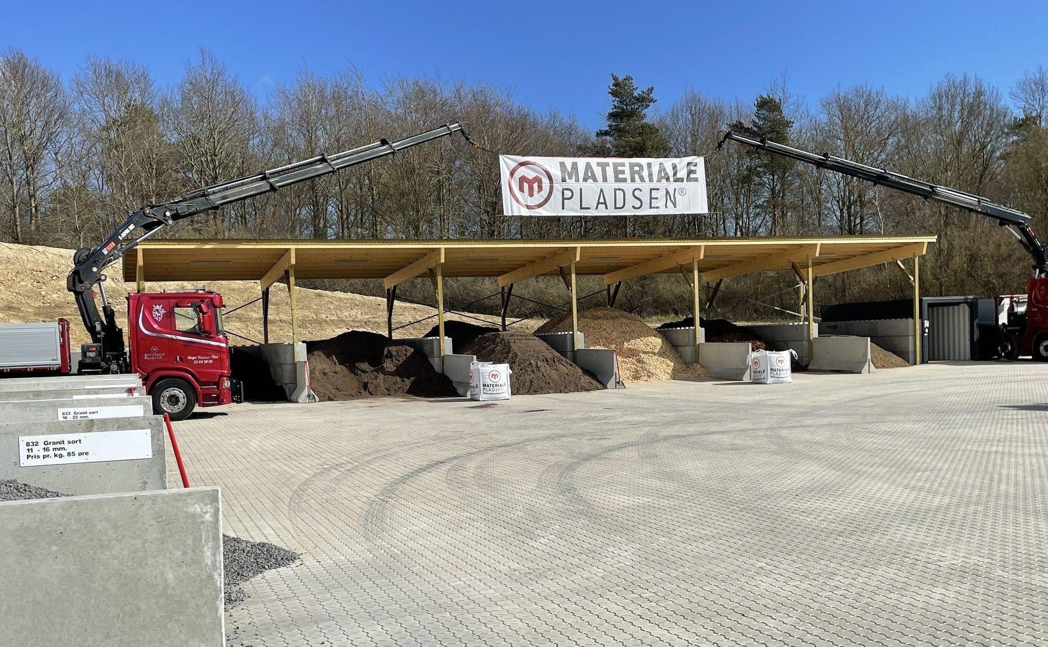 Lagerplads med overdækning til materialer, lastbiler og containere på Materialepladsen i solrigt vejr.