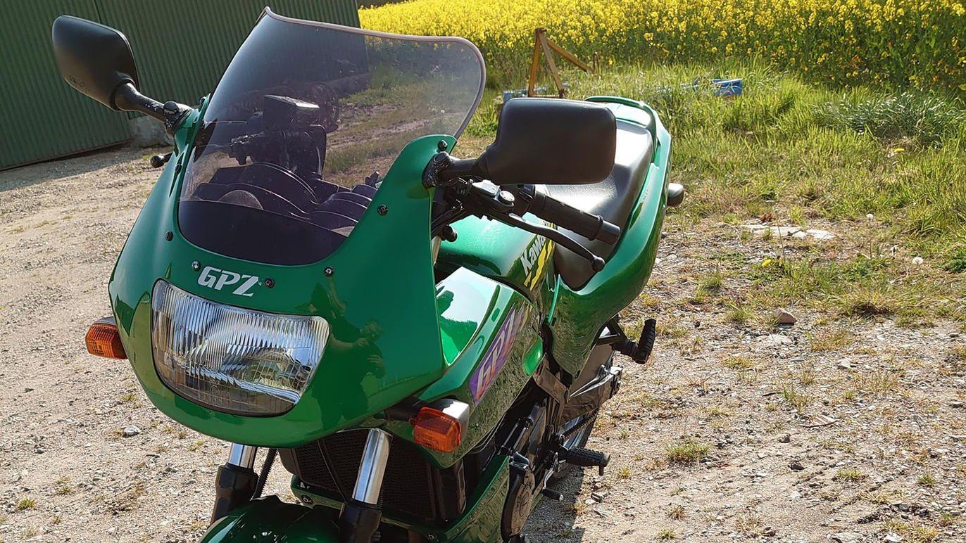 En grøn motorcykel med GPZ-mærkning står på en grusvej med en blomstrende mark i baggrunden.