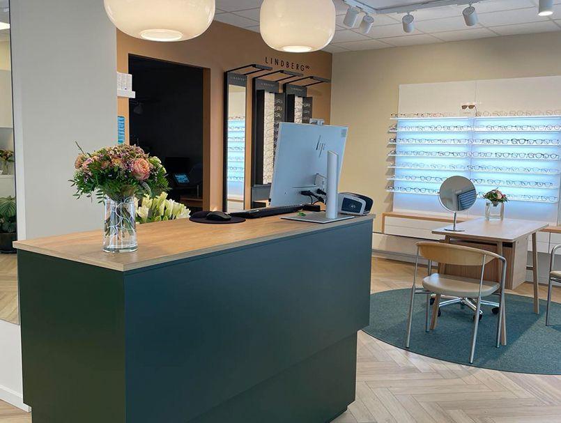 Modtagelsesområde med en grøn skranke, blomster i vase og moderne møbler i et lyst rum.