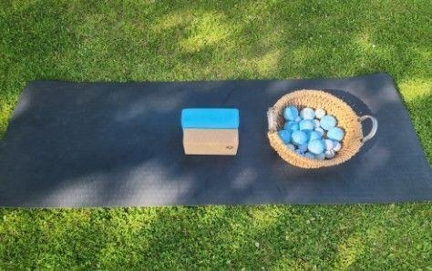 En yogamåtte med en yogaklods og en kurv fyldt med farverige bolde på græsset.