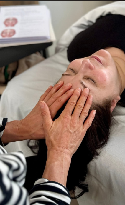 En kvinde får ansigtsmassage, mens hun ligger på en behandlingsbriks med lukkede øjne.