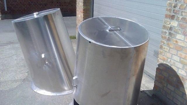 En åben metalcontainer med en rund top, placeret på en asfaltbelagt overflade.