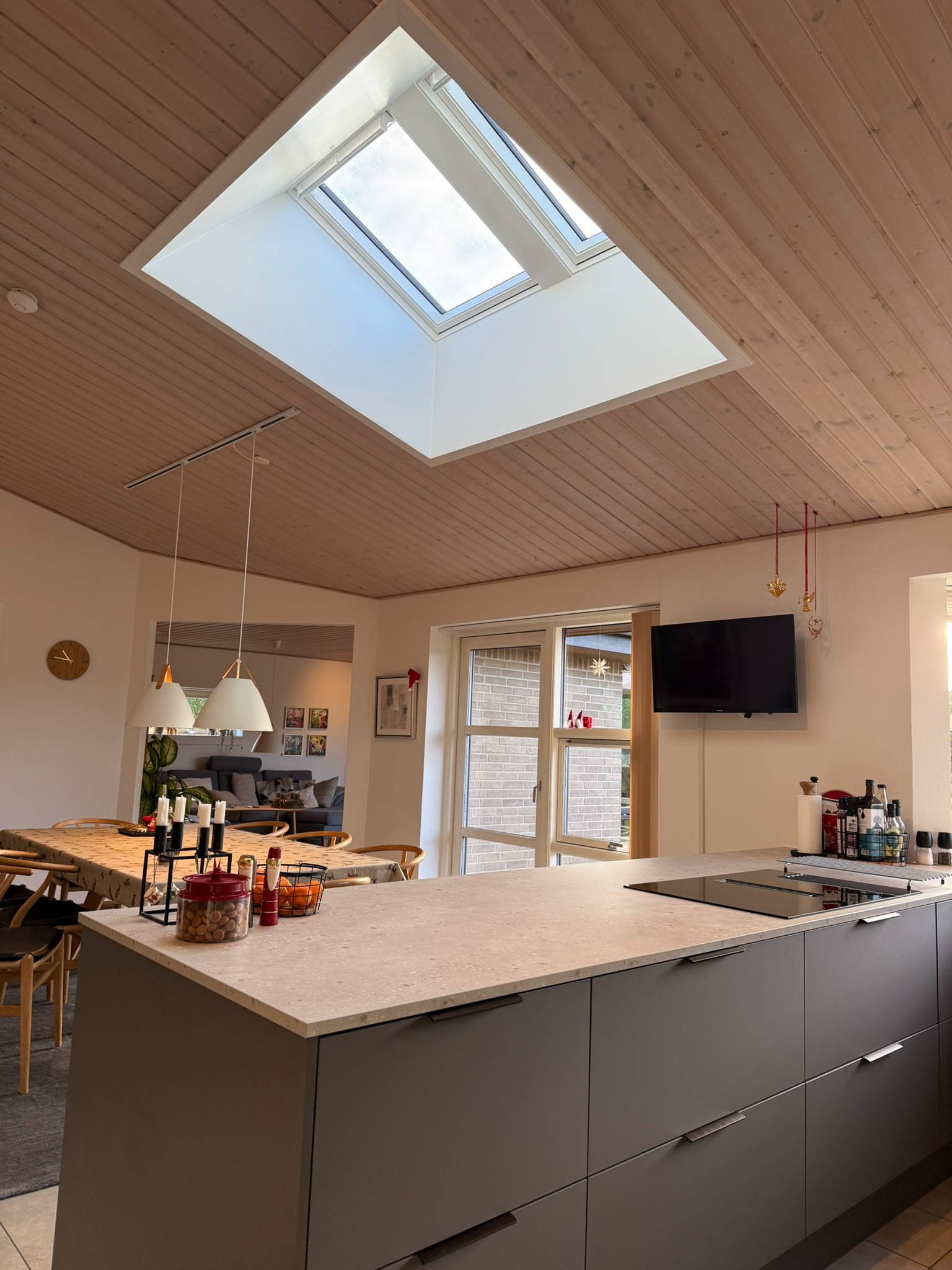 Moderne køkken med ovenlysvindue, grå køkkenø og spiseplads i baggrunden.