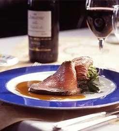 Lækker tallerken med grillet laks, grønne asparges og en rødvin i baggrunden.