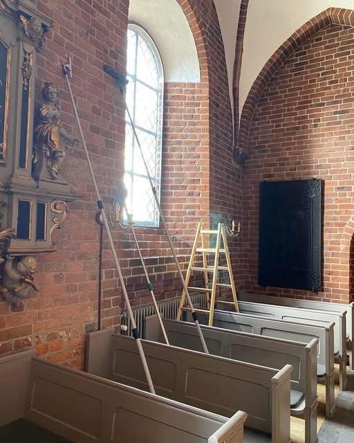 Inde i en kirke med murstensvægge, bænke og en stige ved vinduet.