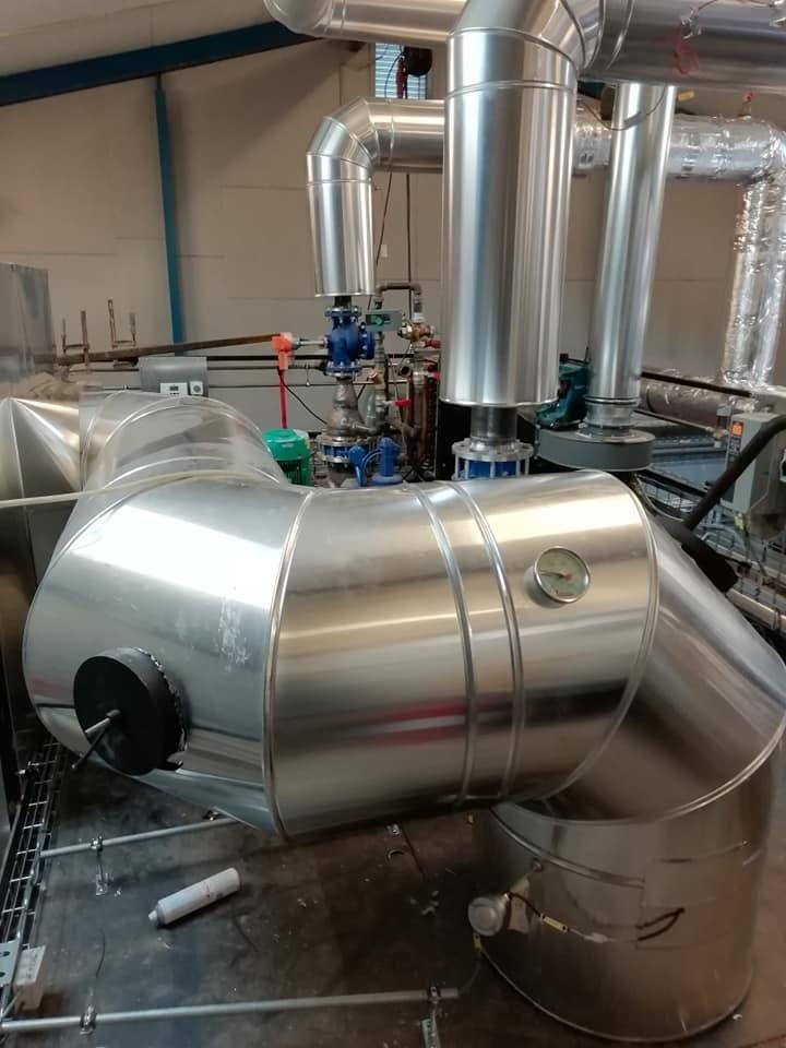 Billede af metalrør og fittings i et industrielt anlæg med synlige ventiler og tilslutninger.